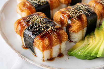 Katsu musubi with crispy breaded cutlet, rice, nori and teriyaki glaze, served with sliced avocado